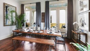 A dining area with a long wooden table set for six, flanked by dark curtains and a large mirror.