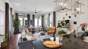 A spacious living room with a dark wood floor, a large sofa, a dining area, and a kitchen island with a candle and snacks.