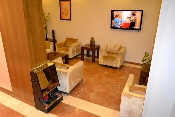 A lobby with a marble floor, a television mounted on the wall, and several armchairs and a sofa.
