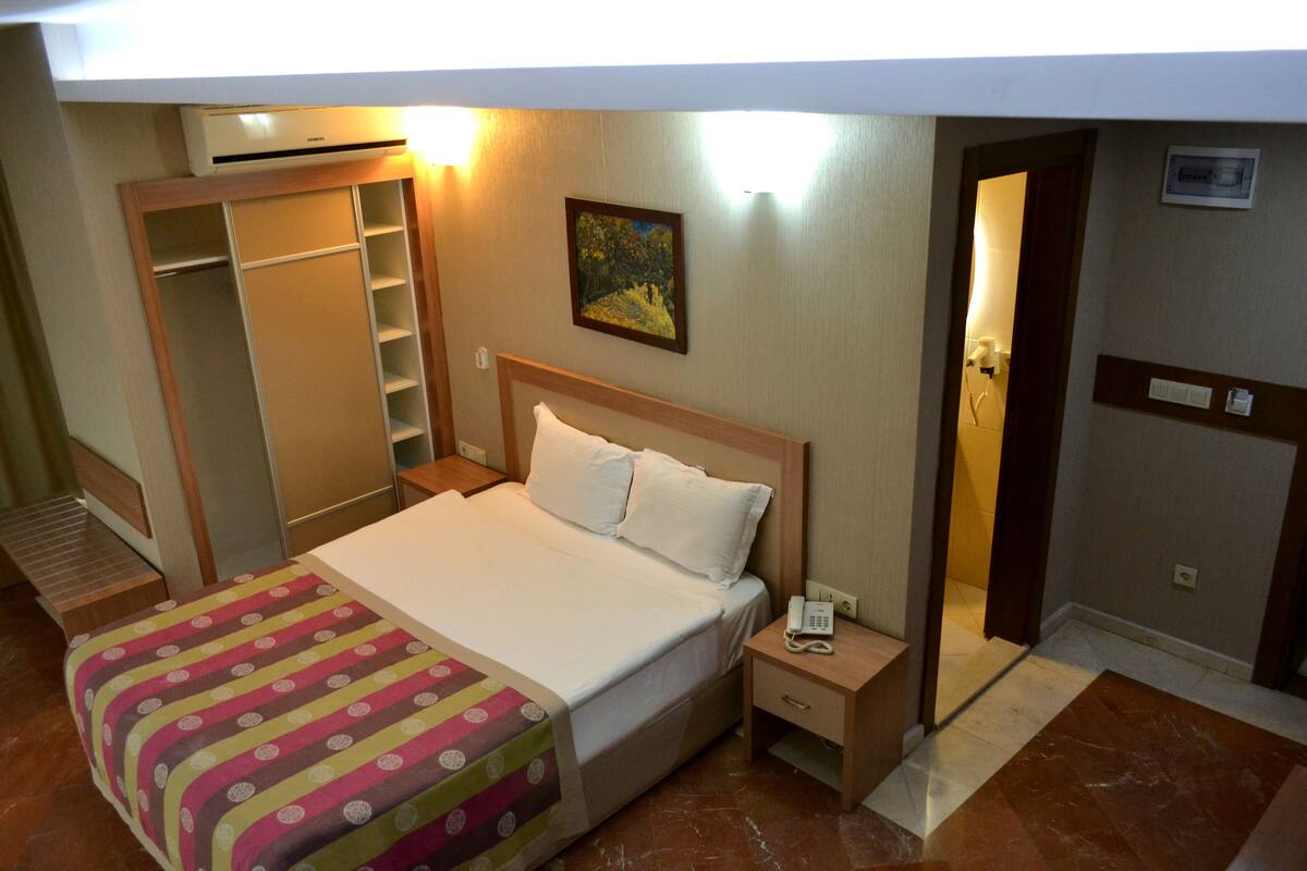 A hotel room with a bed, bedside table, and a wardrobe.