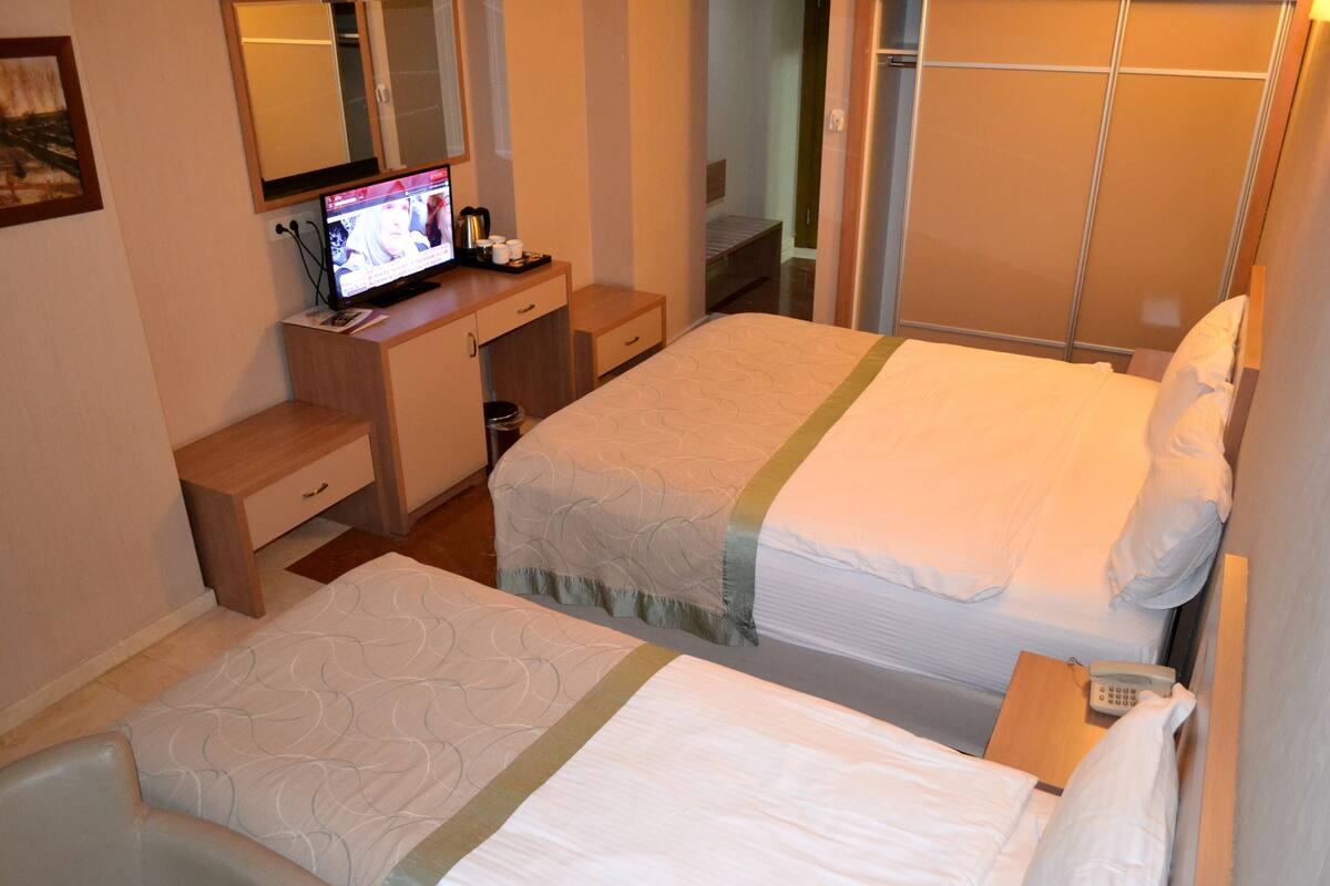 A hotel room with two beds, a desk with a computer, and a wardrobe.