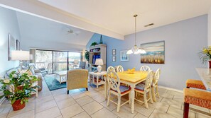 A spacious living area with a dining table, chairs, and a sofa. There is a bookshelf and a plant in the room.