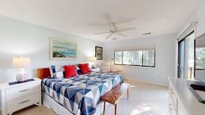 A bedroom with a bed, bedside tables, a bench, a ceiling fan, a window, and a TV.