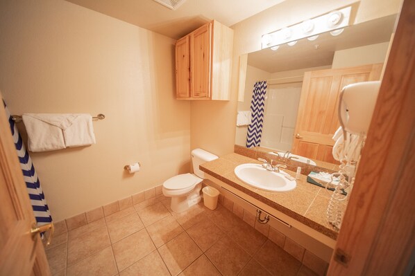 A bathroom with a toilet, sink, mirror, and wooden cabinets.