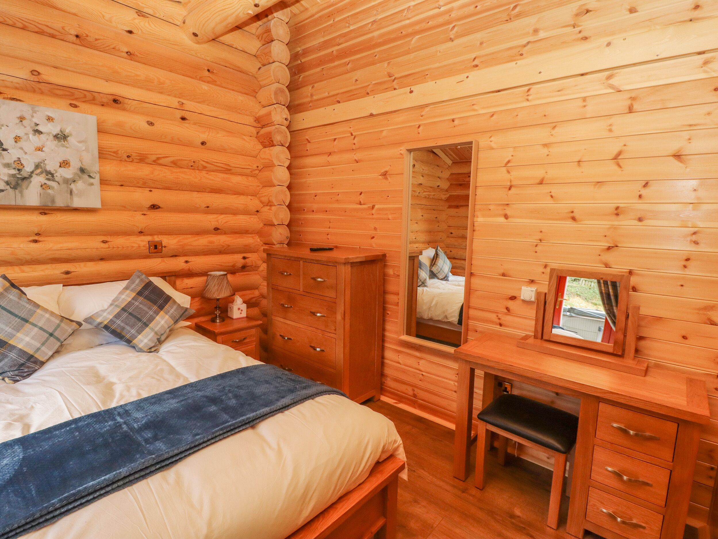 Un dormitorio de cabaña de madera con cama, cómoda, espejo y un cuadro en la pared.