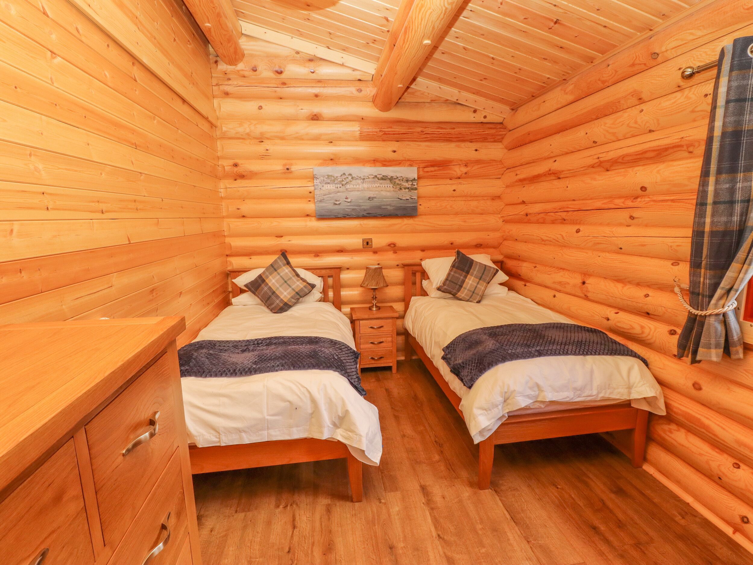 A cabin with two wooden beds, a wooden dresser, and a painting on the wall.