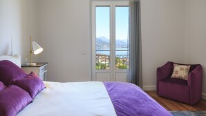 Et soveværelse med seng, et natbord, en lampe, en lilla stol og en balkon med udsigt til bjerge.