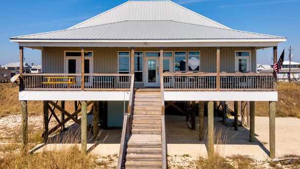 Una casa en la playa con terraza de madera, porche cubierto y vista al océano.