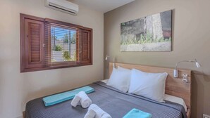 Een slaapkamer met een bed, een raam met zonwering, een schilderij aan de muur en een bedlampje.