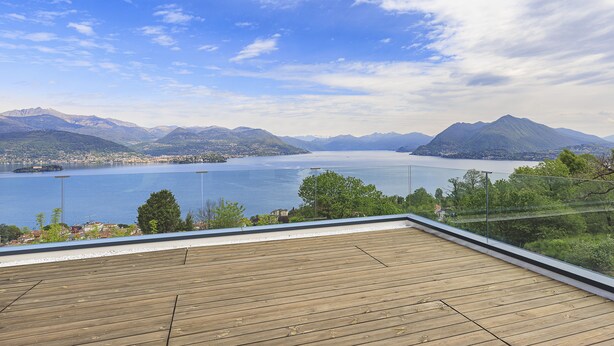 A wooden deck with a glass railing overlooking a lake and mountains. - Skylake Penthouse - Stresa  (Stresa)