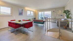 A spacious living area with a dining table, red chairs, a sofa, and a staircase. - Skylake Penthouse - Stresa  (Stresa)