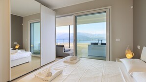 A modern hotel room with a large bed, a balcony with a view of the mountains, and a separate seating area with a table and chairs. - Skylake Penthouse - Stresa  (Stresa)