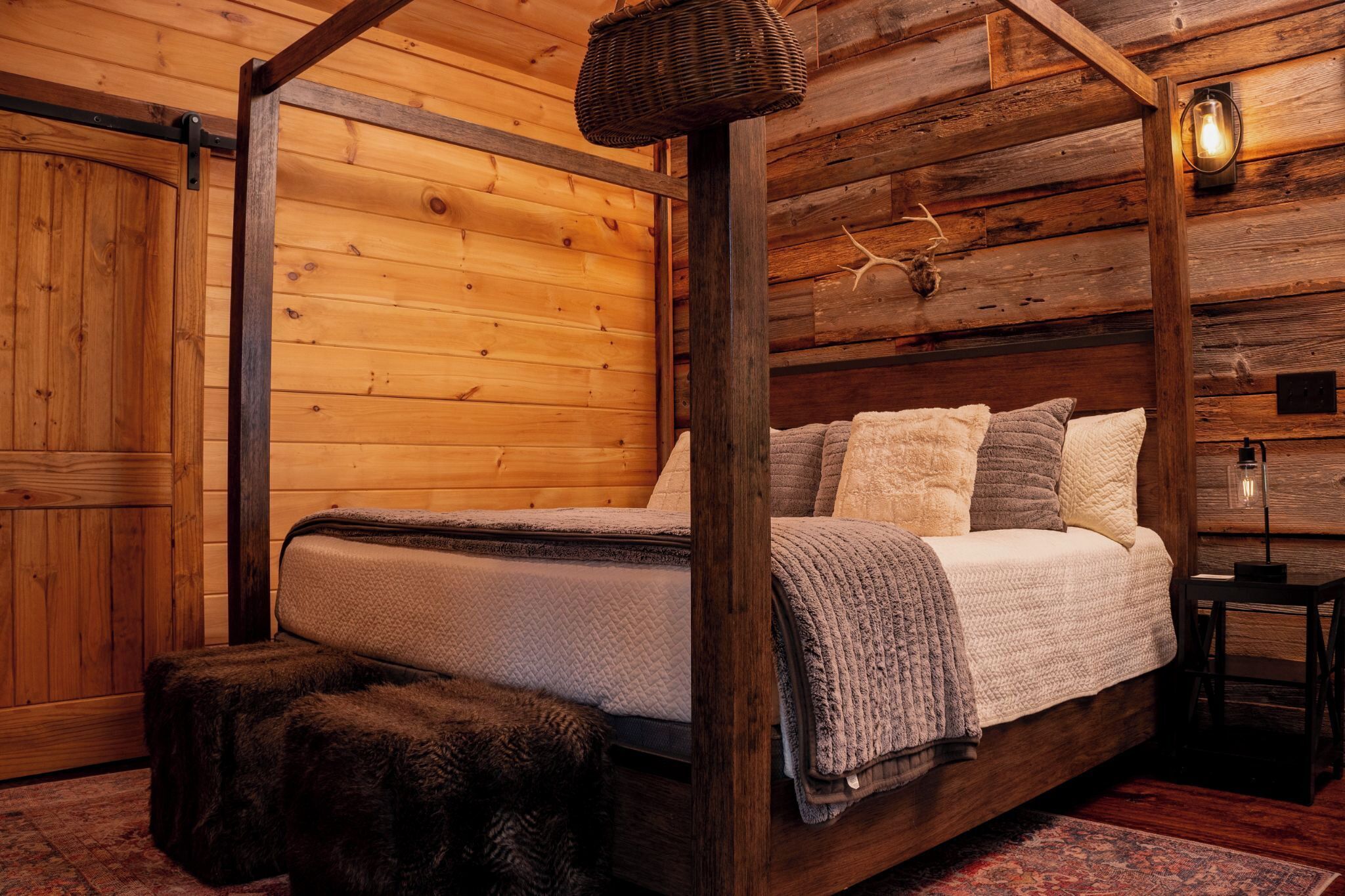 A wooden cabin-style bedroom with a four-poster bed, a small table, and a lamp.