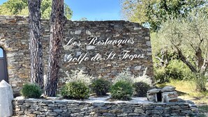 Eine Steinsäule mit dem Schriftzug "Les Postesques Gaffe de St Tropez" und umgebendem Grün.