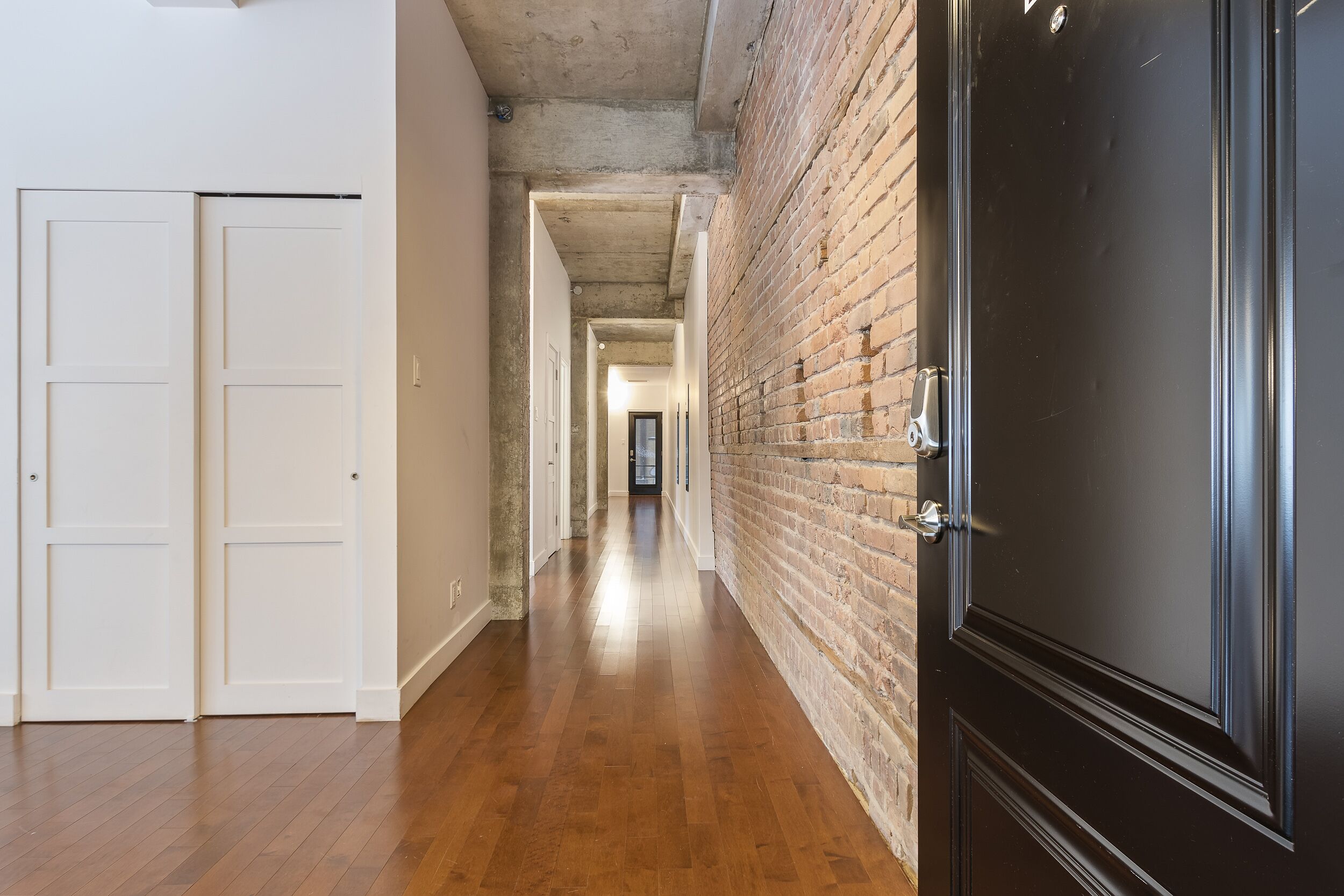 Un couloir avec un plancher en bois, des portes blanches et un mur en briques.