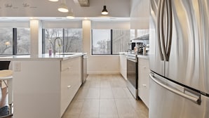 Una cocina moderna con refrigerador de acero inoxidable, armarios blancos e iluminación colgante.