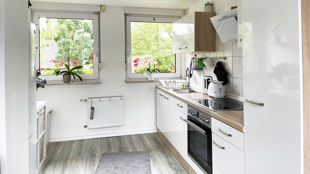 A modern kitchen with white cabinets, a built-in oven, and a window overlooking a garden. - Tammens "Naturblick" - comfortable and beautiful (Papenburg)