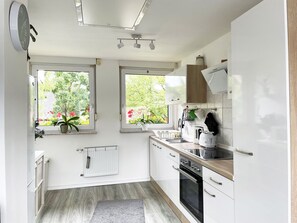 A modern kitchen with white cabinets, a built-in oven, and a window overlooking a garden. - Tammens "Naturblick" - comfortable and beautiful (Papenburg)