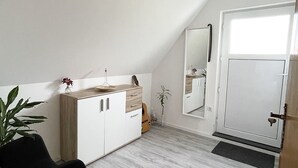 A modern, well-lit room with a white ceiling, a wooden cabinet with drawers, a black chair, a guitar, and a door with a mirror. - Tammens "Naturblick" - comfortable and beautiful (Papenburg)