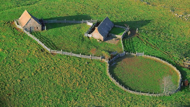 Ein Bauernhaus aus Stein mit einem umzäunten Hof und einer kreisrunden Steinmauer.