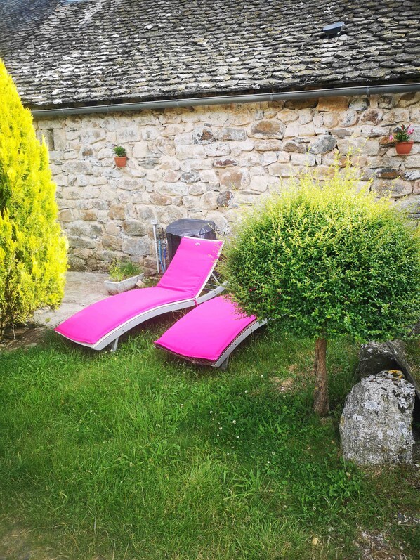 A stone building with a tiled roof, two lounge chairs with pink cushions, a small bush, and a potted plant on the wall. - Escape the heat wave at La Grange de Melaual, (Soulages-Bonneval)