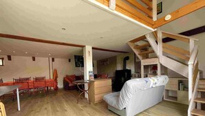 Ein geräumiger Wohnbereich mit Holzboden, einer Couch, einem Esstisch mit Stühlen, einer Treppe und einem Kamin.