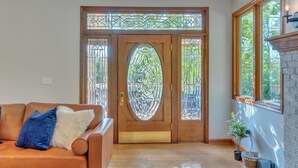 A room with a wooden door with stained glass, a fireplace, a couch with pillows, and a potted plant. - 5 BR Wintergreen House w/ Game Room, 75” TV, Ping Pong, Foosball, Wet Bar & Deck (Nellysford)