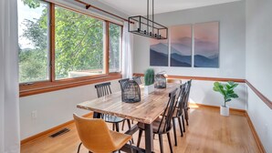 A dining area with a wooden table, chairs, and a view of trees through large windows. - 5 BR Wintergreen House w/ Game Room, 75” TV, Ping Pong, Foosball, Wet Bar & Deck (Nellysford)