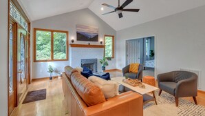 A spacious living room with a fireplace, a ceiling fan, and large windows. - 5 BR Wintergreen House w/ Game Room, 75” TV, Ping Pong, Foosball, Wet Bar & Deck (Nellysford)
