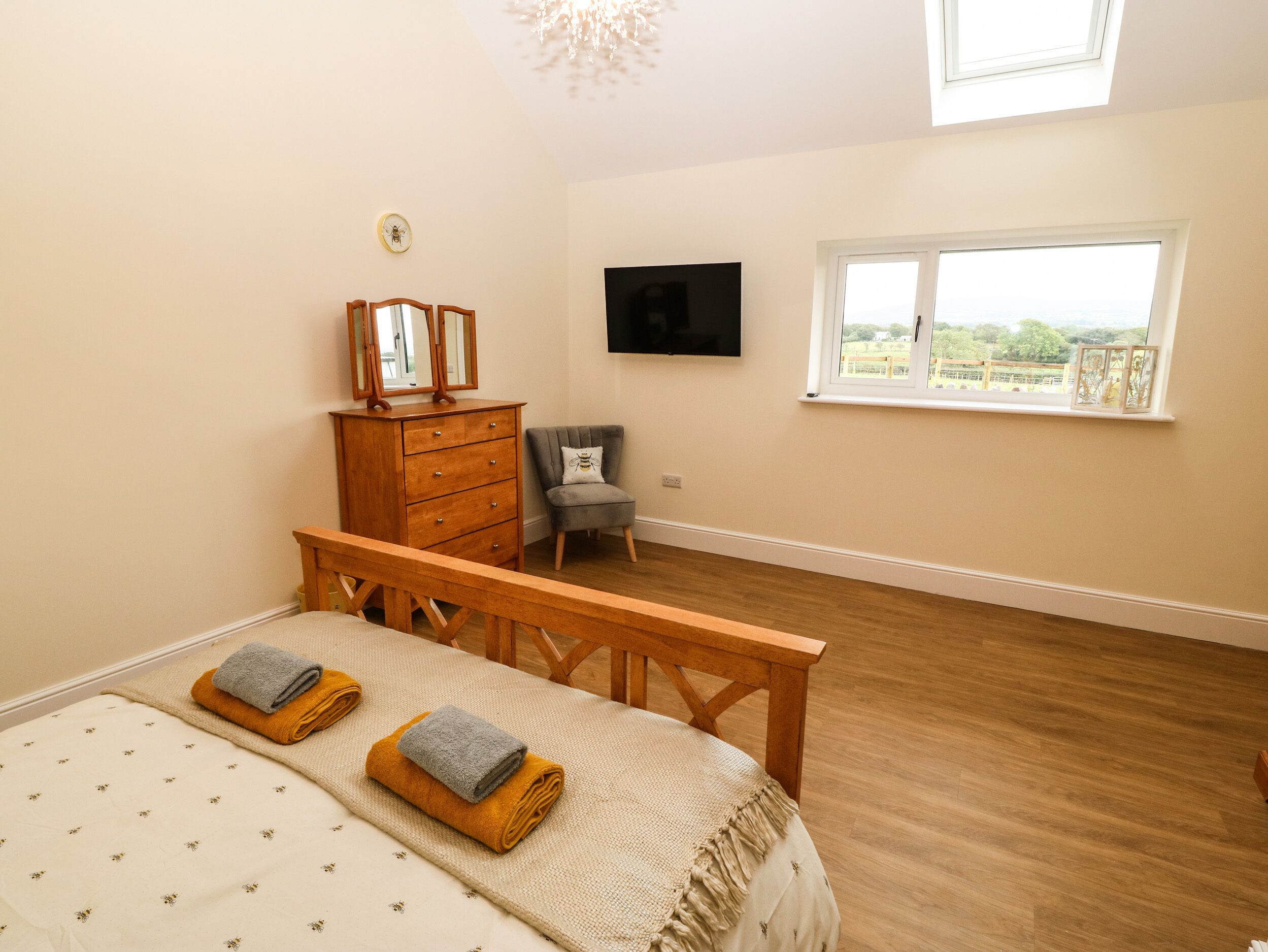 A bedroom with a bed, wooden dresser, TV, and a window with a view.
