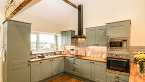 Een moderne keuken met grijze kastjes, een houten aanrecht, een ingebouwde oven en een raam met uitzicht op groen.