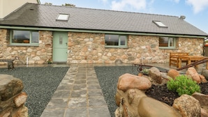 Een stenen huis met een betegelde ingang, een groene deur en een klein terras met een tafel en bank.