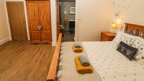 Een slaapkamer met een houten bed, een nachtkastje met een lamp, een kledingkast en een zichtbare badkamer door een geopende deur.