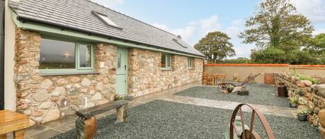 A stone building with a tiled roof, a gravel patio, and a wooden bench.