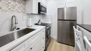 Una cocina moderna con armarios blancos, un refrigerador de acero inoxidable, un microondas y una tetera sobre la encimera.