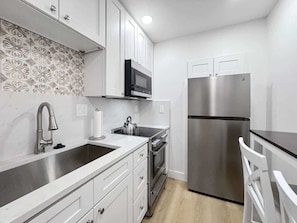 A modern kitchen with white cabinetry, a stainless steel refrigerator, a microwave, and a kettle on the countertop.