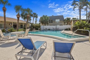 A pool area with lounge chairs, palm trees, and a building in the background.
