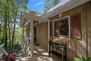 A wooden porch with a railing, a window with shutters, and a table with flowers.