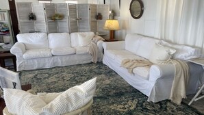 Une pièce avec deux canapés blancs, un tapis à motifs et un fauteuil en osier.