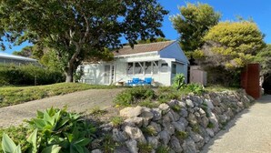 Une maison avec un mur en pierre, une véranda avec des chaises bleues et un jardin avec des plantes vertes.