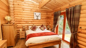 Une chambre à coucher dans une cabane en bois, avec un lit, une commode, une table de chevet, une lampe et un tableau encadré au mur.