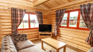 L’intérieur d’une cabane en rondins, avec un canapé, un téléviseur posé sur un meuble en bois et des rideaux à carreaux.