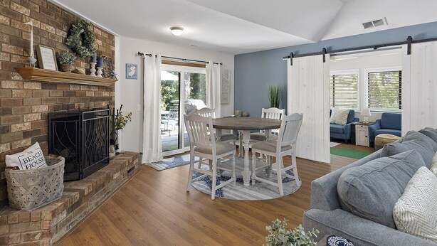 Un salon avec une cheminée, une table à manger avec des chaises, un canapé et une grande fenêtre avec des stores.