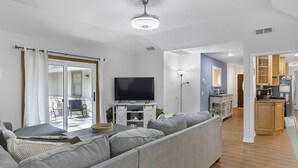 Un salon moderne avec un canapé gris, un téléviseur à écran plat et un coin repas doté de meubles en bois, avec une cuisine en arrière-plan.