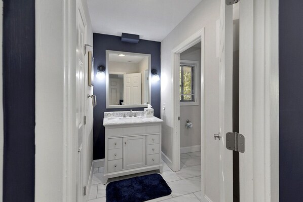 Un baño estrecho con tocador blanco, un espejo grande y una pared azul oscuro como detalle.