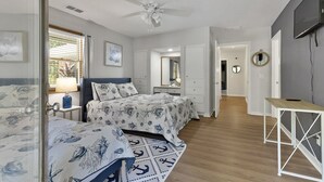 Une chambre à coucher comprenant un lit, des tables de chevet, un ventilateur de plafond, une télévision et un bureau.