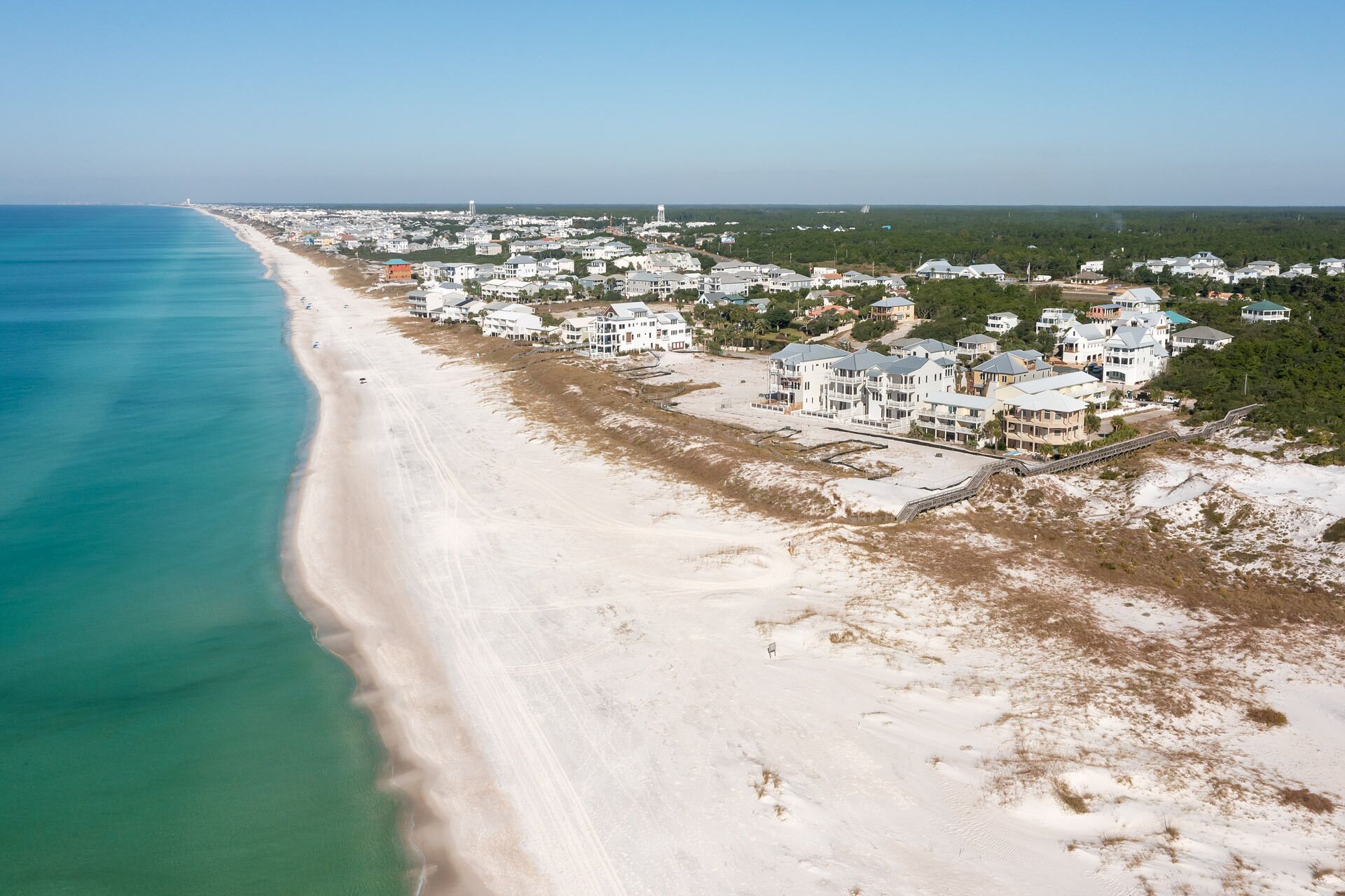 Un quartier résidentiel situé sur la côte, avec des propriétés donnant sur la plage, une plage de sable et une vue dégagée sur l’océan.