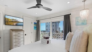 Une chambre avec un lit, une commode, un ventilateur de plafond, une télévision et un balcon avec vue sur l’océan.