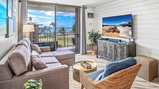 Ein modernes Wohnzimmer mit einer Couch, einem Korbsessel, einem Couchtisch, einem Fernseher und einem Balkon mit Meerblick.