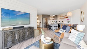 Ein modernes Wohnzimmer mit großem Fernseher, einer Couch, einem Couchtisch und einer Küche im Hintergrund.